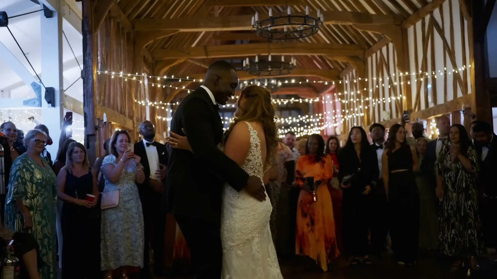 A first dance in a fairy-lit barn, guests gathered around